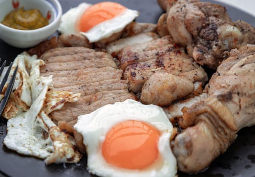 Close-up of Sliced ​​pork steak, Fried chicken drumsticks and Fried eggs for dinner are served with dipping sauce on ceramic plate. A plate of favorite food, Space for text, Selective Focus.