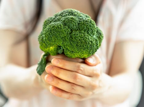 The lady is holding fresh green broccoli and giving it to the camera. Healthy eating concept, Space for text, Selective focus.