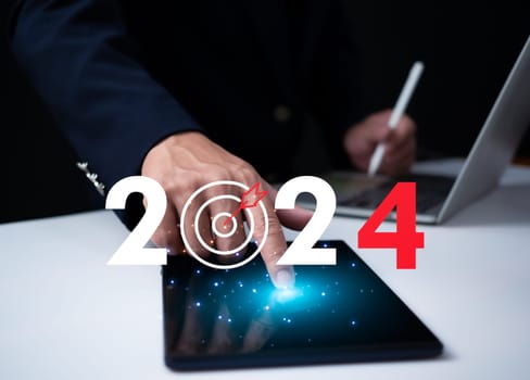 Businessman pointing at tablet showing dartboard icon with numbers Represents goal setting for 2024. Startup concept, financial planning, development strategy, business goal setting,