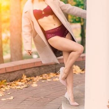 Young beautiful dark-haired woman with a slender figure posing in lingerie and a classic coat in an autumn park