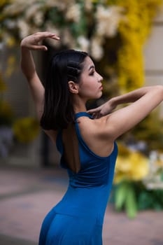 Close-up portrait of a beautiful Asian ballerina posing against the background of a building decorated with flowers. Vertical photo