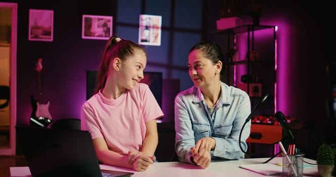 Daughter and mother filming reaction video for gen Z audience, preparing to look at online videos on laptop. Cute kid and her parent recording reaction to internet clips for family channel