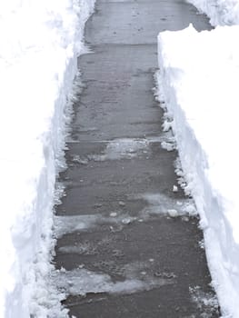 A solitary pathway cuts through a blanket of snow in a quiet residential neighborhood, leading to a welcoming home. The overcast sky and untouched snowdrifts capture the stillness of a winter day.