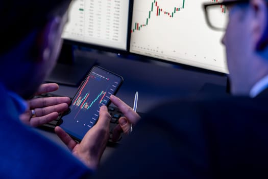 Two stock exchange traders researching data on smartphone and laptop screen server of dynamic digital currency. Investors analyzing market stock at decorative neon blue-light of workplace. Sellable.