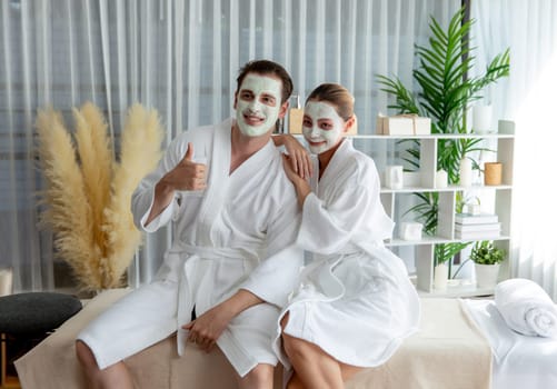 Blissful couple in bathrobe with facial cream mask enjoying serene ambiance of spa salon resort or hotel during holiday. Pampering face spa and skincare treatment with essence relaxation. Quiescent