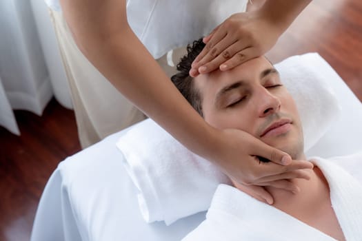 Caucasian man enjoying relaxing anti-stress head massage and pampering facial beauty skin recreation leisure in dayspa modern light ambient at luxury resort or hotel spa salon. Quiescent