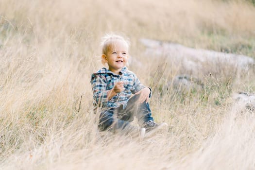 Little happy girl sits in dry grass on the lawn. High quality photo