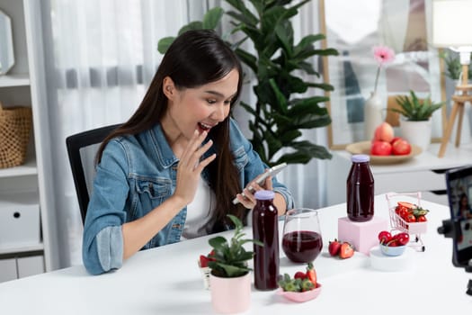 Smiling young beautiful Asian reviewing tasty mixed strawberry and cherry juice detox drinks, showing healthy product to promote for special promotion selling on social media online record. Stratagem.