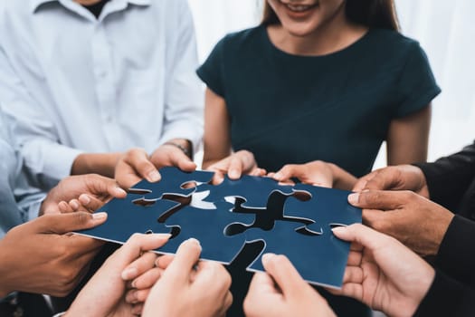 Diverse corporate officer workers collaborate in office, connecting puzzle pieces to represent partnership and teamwork. Unity and synergy in business concept by merging jigsaw puzzle. Concord