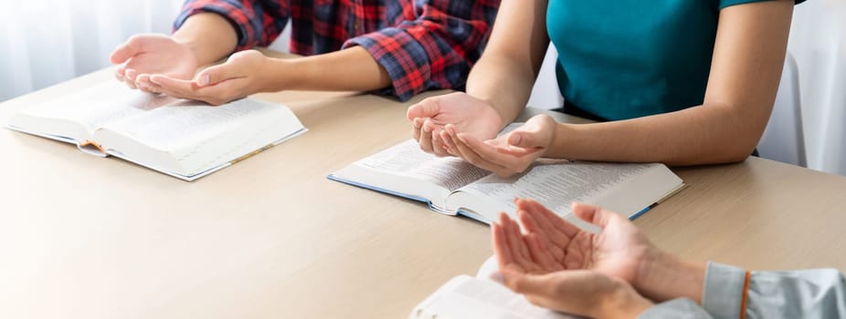 Cropped image of diversity people hand praying together at wooden church on bible book. Group of believer hold hand together faithfully. Concept of hope, religion, faith, god blessing. Burgeoning.