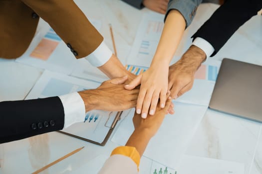 Top view of corporate diverse businesspeople putting hands together on meeting table with document scatter around at business meeting room. Represented unity, cooperation, collaboration. Ornamented.