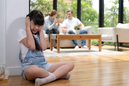 Stressed and unhappy girl huddle in corner, cover her ears with painful expression while her parent arguing in background. Domestic violence and traumatic childhood develop to depression. Synchronos