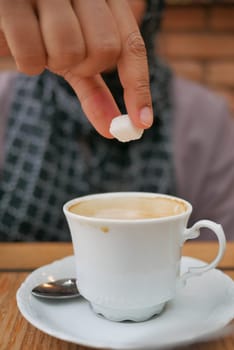 woman hand pouring white sugar cube in a coffee cup ,.