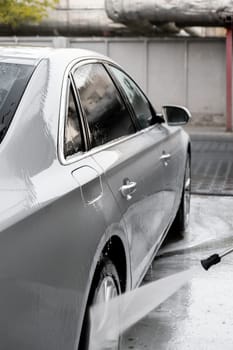 Washing luxury silver car on touchless car wash. Washing sedan car with foam self-service and high pressure water. Cleaning the details of car. Cleanliness and order in urban environment