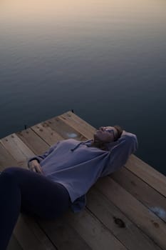 Woman lying down on the pier at lake, closeup portrait, summer sunset