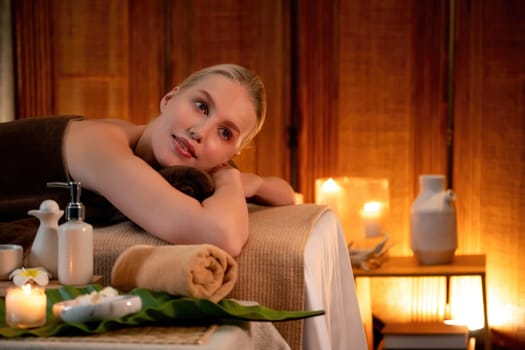 Caucasian woman customer enjoying relaxing anti-stress spa massage and pampering with beauty skin recreation leisure in warm candle lighting ambient salon spa at luxury resort or hotel. Quiescent