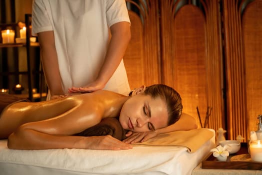 Caucasian woman customer enjoying relaxing anti-stress spa massage and pampering with beauty skin recreation leisure in warm candle lighting ambient salon spa at luxury resort or hotel. Quiescent