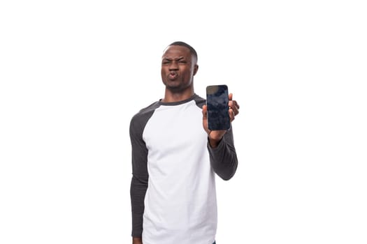 young handsome american man dressed in a long-sleeved sweater demonstrates the screen of a smartphone with a mockup.