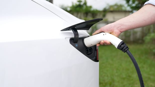 Modern eco-friendly man recharging electric vehicle from home EV charging station. EV car technology utilized for home resident to future environmental sustainability. Synchronos