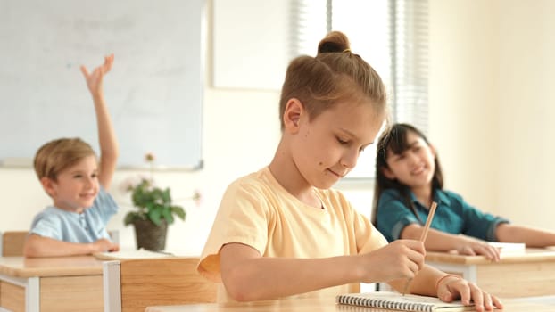 Smart elementary student looking at teacher while attend in classroom. Diverse smart student sitting at classroom while listening teacher explain about classwork or test. Education concept. Pedagogy.