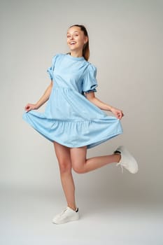 Young happy smiling woman in a light blue dress on a gray background close up