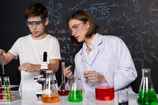 Teacher support schoolboy in laboratory. Schoolboy and teacher stand and experiment about science of chemistry in STEM class using liquid in glass container. Instructor mixing solution. Erudition.