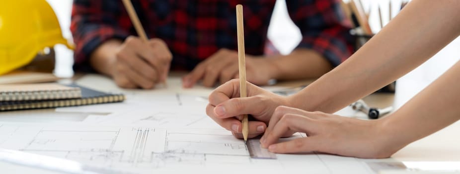 Cropped image of cooperative architect team decide and work together on meeting table with house model, safety helmet and architectural plan scatter around. Closeup. Focus on hand. Burgeoning.