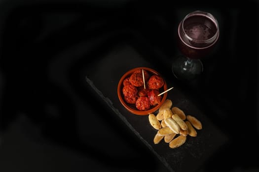 top view of an earthenware casserole with fried sausage, bread and a glass of wine isolated on a black background.