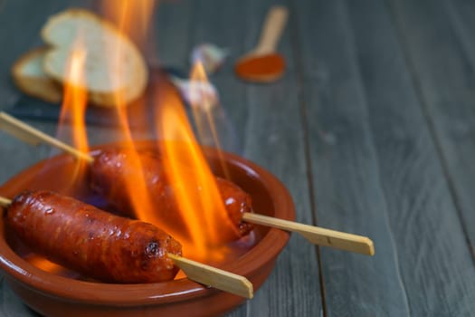 typical spanish tapa ,chorizo on fire in an earthenware casserole with slices of bread in the background.