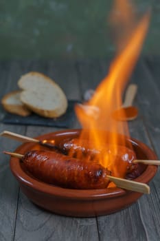typical spanish tapa ,chorizo on fire in an earthenware casserole with slices of bread in the background.