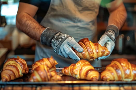 A closeup shot of a baker holding freshly made croissant in his gloved hand.