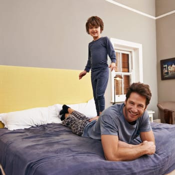 Happy, jumping and father with kid on bed bonding, playing and having fun together at modern home. Laughing, smile and boy child standing on dad laying in bedroom on weekend at family house in Canada.
