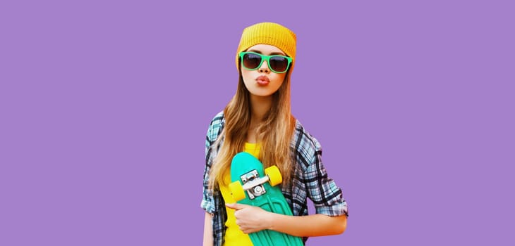 Summer portrait of happy blonde young woman posing with skateboard in colorful clothes on purple studio background