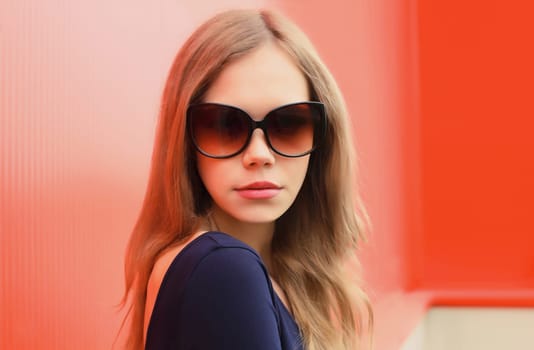Portrait of beautiful young blonde woman posing in black sunglasses looking at camera on red background