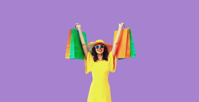 Stylish beautiful happy young woman model with shopping bags in summer straw hat on purple studio background