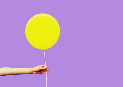 Colorful image close up female hand holding or showing yellow balloon on violet background
