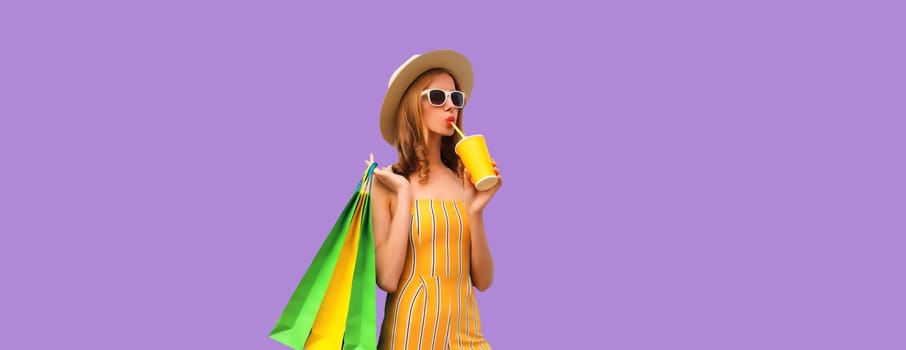 Portrait of stylish beautiful young woman posing with shopping bags drinking coffee or juice in summer hat on purple studio background