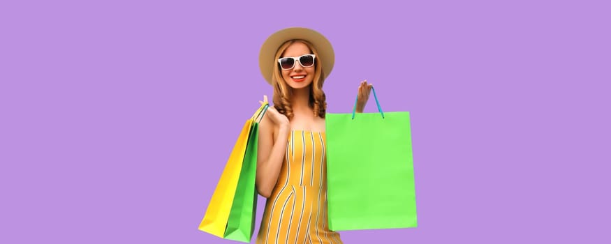 Stylish beautiful happy young woman model with shopping bags in summer straw hat on purple studio background