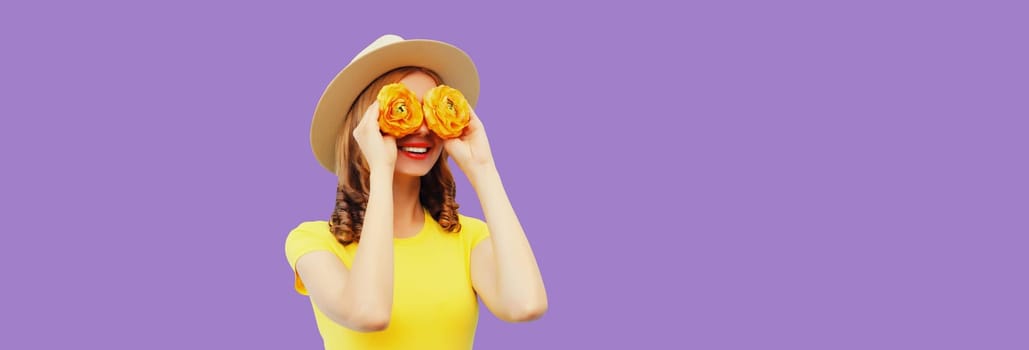 Summer portrait of happy smiling woman covering her eyes with flower buds as binoculars looking for something in straw hat on purple studio background