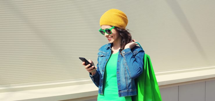 Happy smiling young woman looking at mobile phone with shopping bags on city street