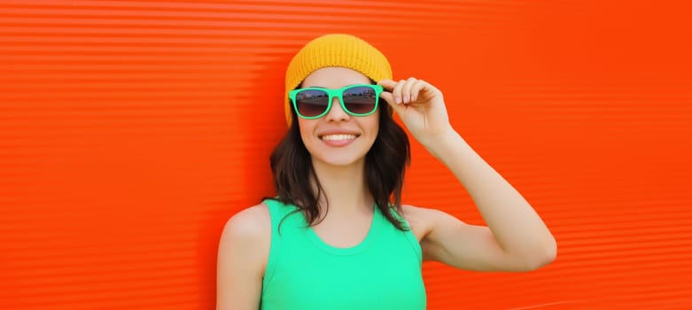 Summer portrait of happy smiling brunette young woman posing in yellow hat, green sunglasses on red background