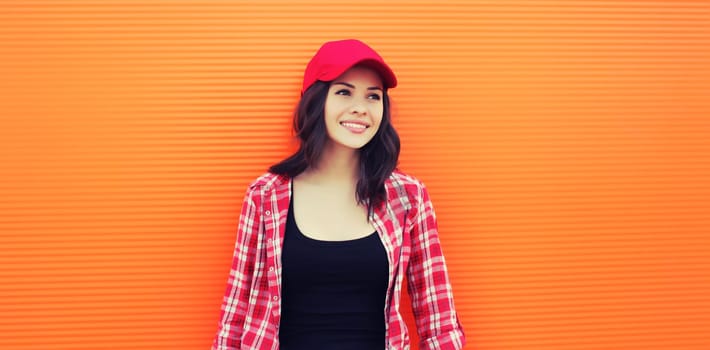 Summer portrait of happy smiling young woman posing in red baseball cap, casual clothes on city street