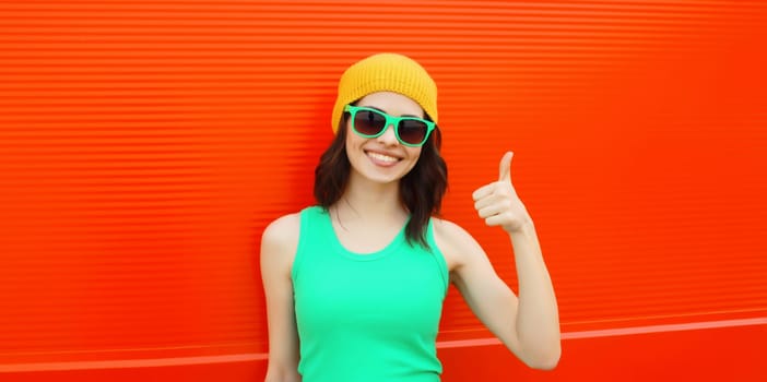 Summer portrait of happy smiling brunette young woman posing in yellow hat, green sunglasses on red background