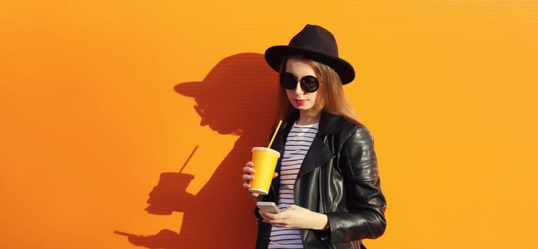 Portrait of modern stylish young woman with mobile phone drinks coffee on colorful orange background in the city