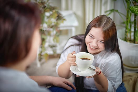 Happy Overweight family with mother and daughter drinking tea or coffee in room. Middle aged woman and teenager girl having fun and joy