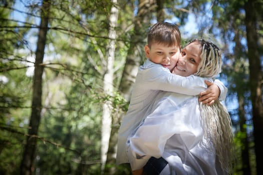 Funny mother with dreadlocks and fat boy happy walking in the forest on a sunny summer day