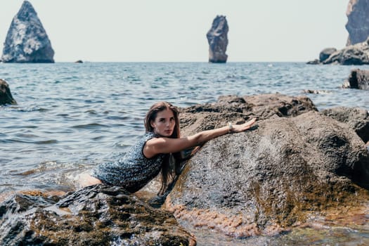 Woman travel sea. Young Happy woman in a long red dress posing on a beach near the sea on background of volcanic rocks, like in Iceland, sharing travel adventure journey