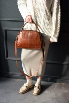 Studio portrait of beautiful woman with a curly blond hair holding brown bag, posing on gray background. Model wearing stylish sweater and skirt