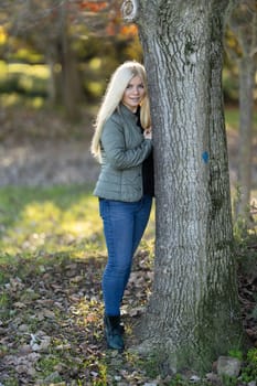 A young woman with braces smiling, leaning against a tree trunk in the woods on a sunny day.