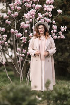 Woman magnolia flowers, surrounded by blossoming trees, hair down, white hat, wearing a light coat. Captured during spring, showcasing natural beauty and seasonal change